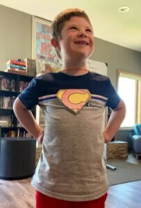 A young camper with a super hero shirt proudly poses in his super hero way