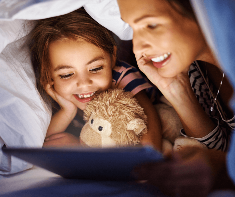 Mom helps daught improve well-being through literacy by reading bedtime story in makeshift tent in the living room.