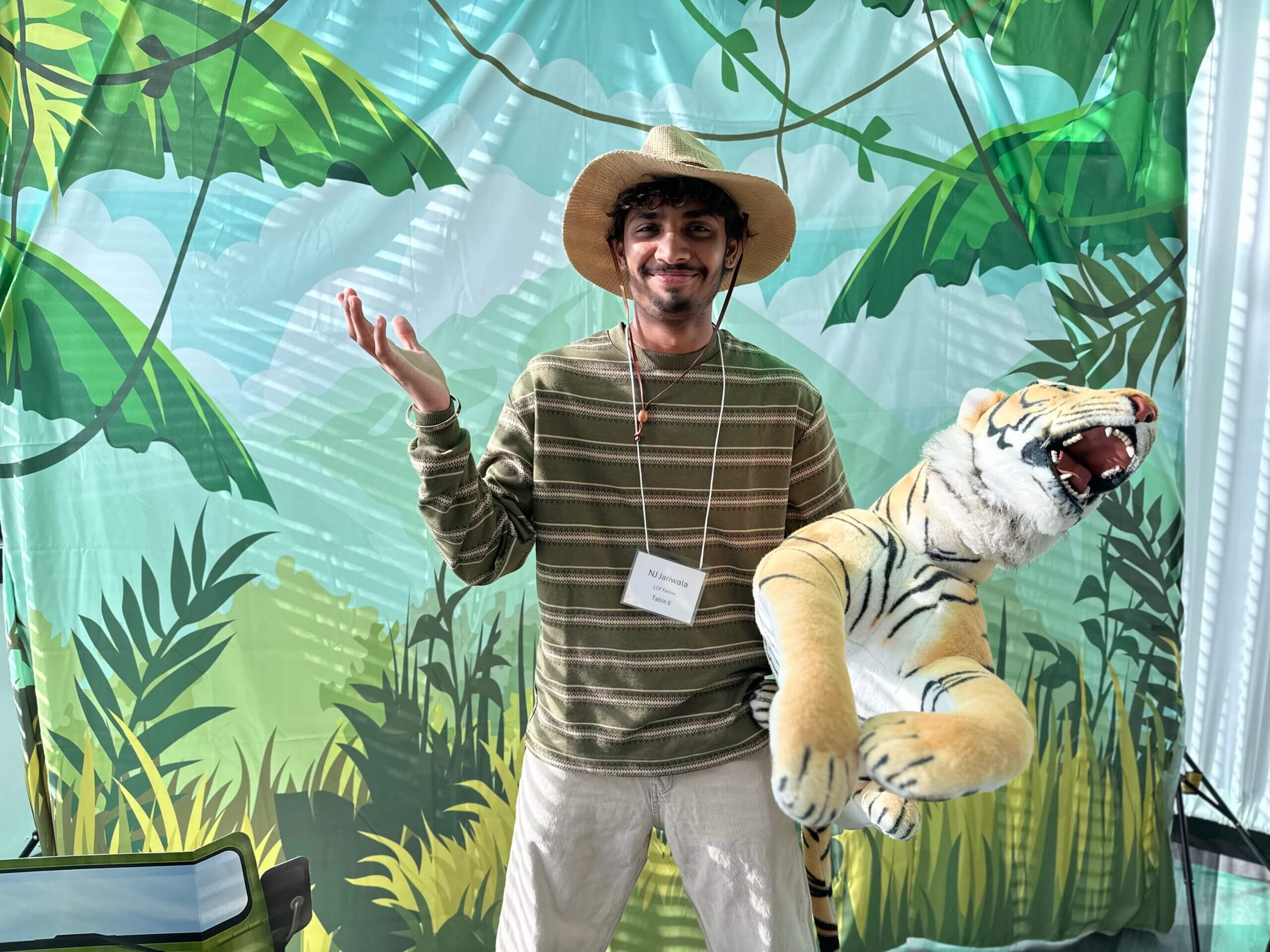 Community Engaged Fellow Nainil “NJ” Jariwala poses for a photo holding a plush tiger with a suitable hat and jungle background.