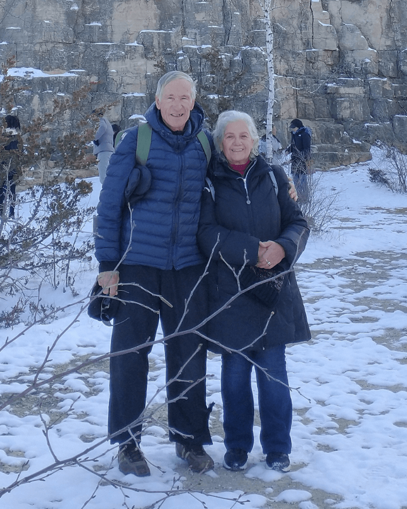 Philanthropiss Bill Katra and Marta Martinez stand in front of a mountain on snow-covered ground.