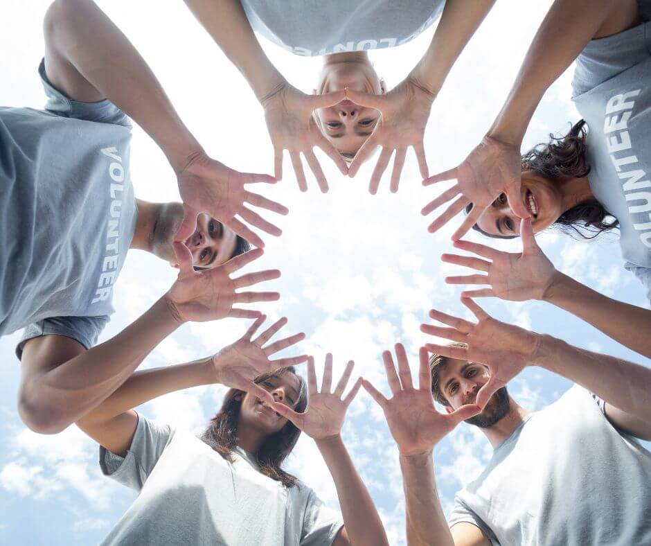 generous volunteers form hands in circle as camera looks up through the circle to a sunlit sky